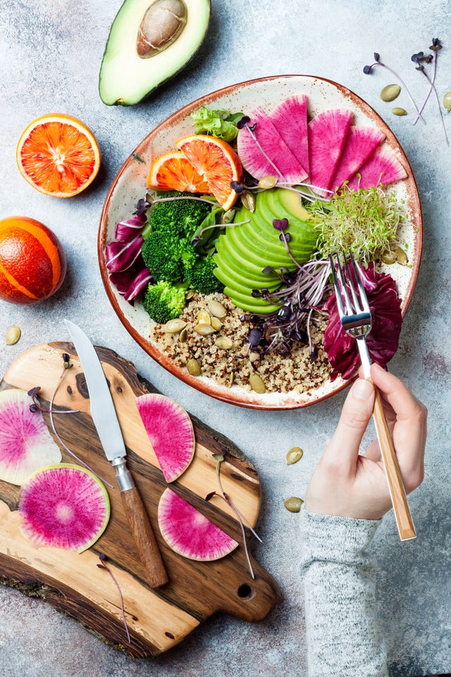 girl holding fork and eating vegan, detox buddha bowl with quinoa, micro greens, avocado, blood orange, broccoli, watermelon radish, alfalfa seed sprouts