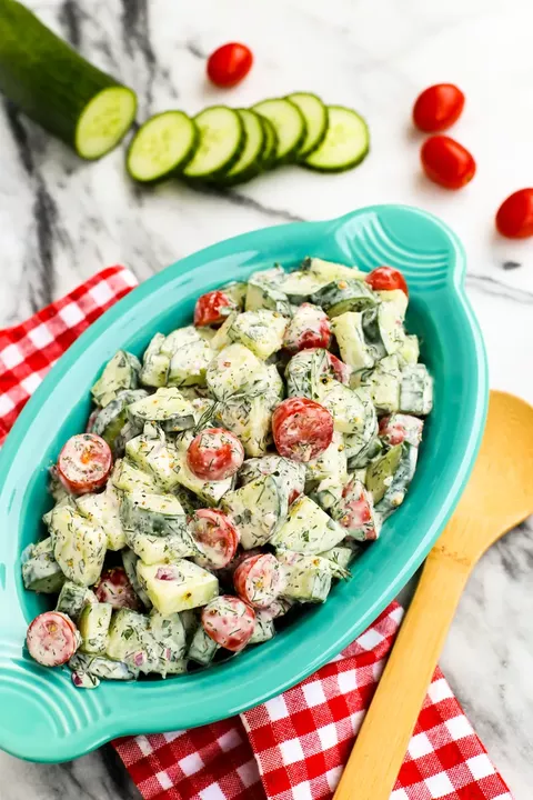 cucumber and tomato salad with creamy herb dressing in blue serving platter wood spoon