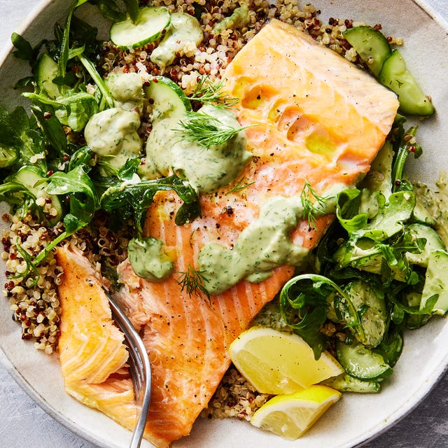 Salmon Quinoa Bowl quinoa in a bowl with salmon, arugula, cucumber, lemon wedges, and a green sauce
