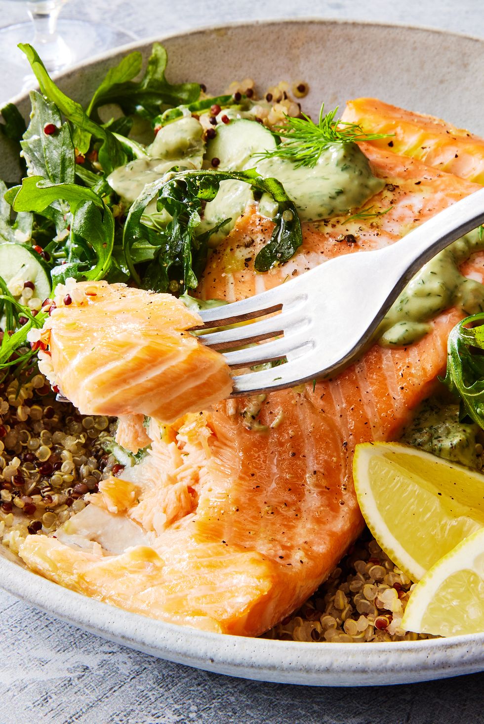 quinoa in a bowl with salmon, arugula, cucumber, lemon wedges, and a green sauce