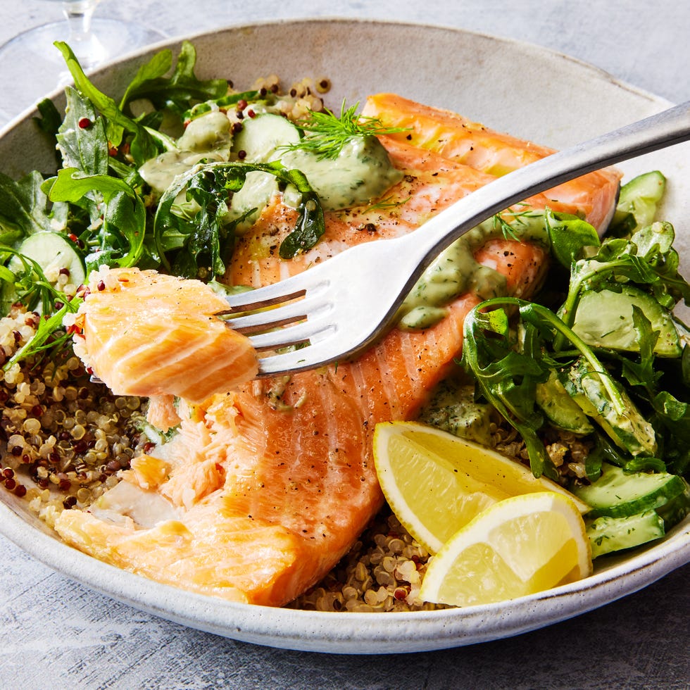 quinoa in a bowl with salmon, arugula, cucumber, lemon wedges, and a green sauce