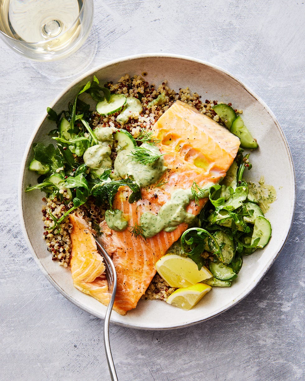 quinoa in a bowl with salmon, arugula, cucumber, lemon wedges, and a green sauce