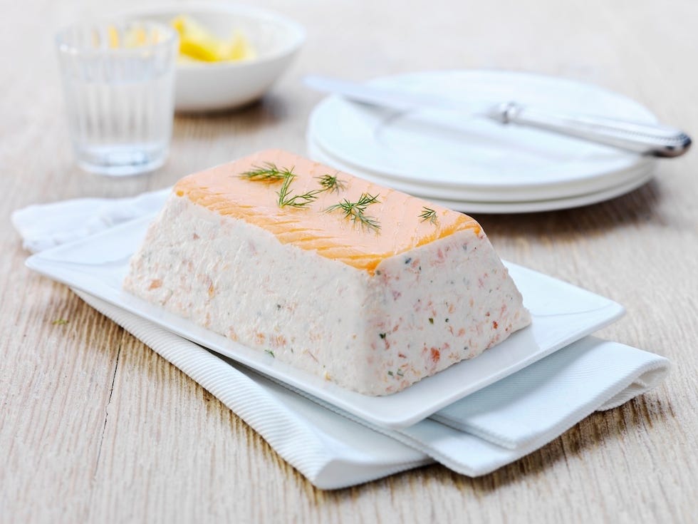 Savory fish terrine displayed on a white platter with garnishes and serving utensils nearby