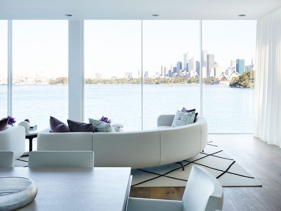 Neutral Bay en Sídney de Greg Natale salon con sofa semicircular y decoracion en blanco y morado frente a un ventana con vistas a la opera de sidney