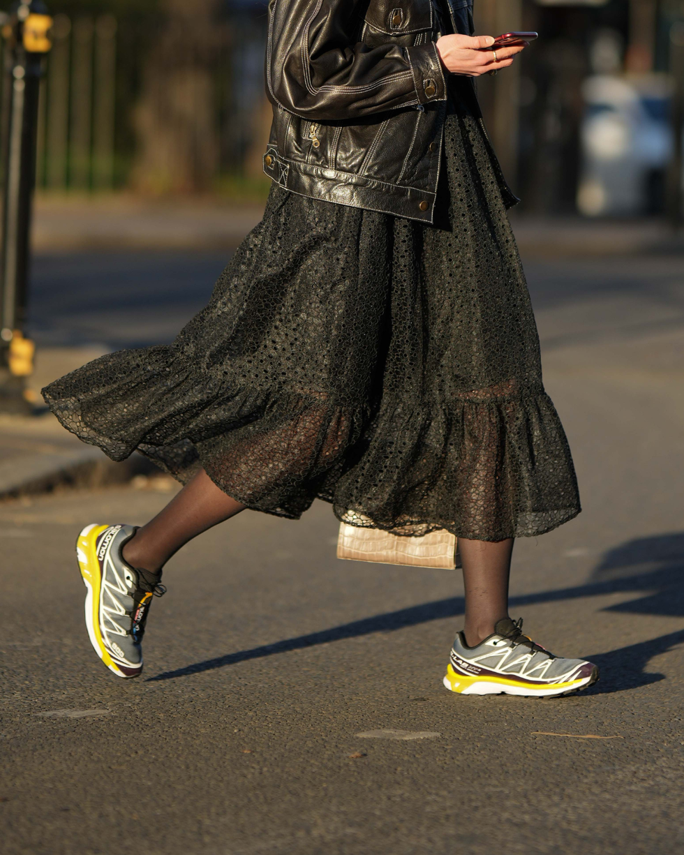 a person walking wearing a black layered skirt and a leather jacket with athletic shoes