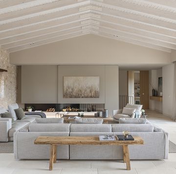 un salon de campo con chimenea, sofas grises, techos a dos aguas y pared de piedra