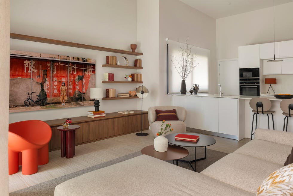 salón con mueble de tv de madera, butaca beige y silla de color naranja frente a mesas de centro tipo nido