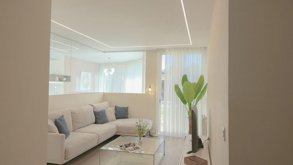 salón abierto a la cocina con sofá con chaiselongue y mesa de centro de cristal