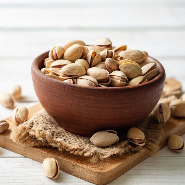 Salted pistachio nuts in ceramic bowl on white wooden background