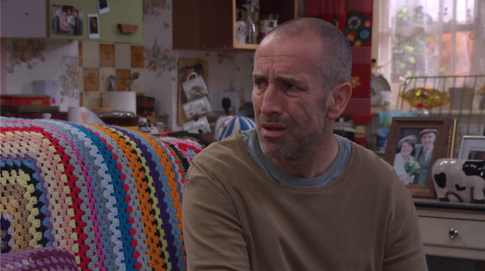 sam dingle looking puzzled as he sat on the sofa on a colourful crocheted blanket on emmerdale