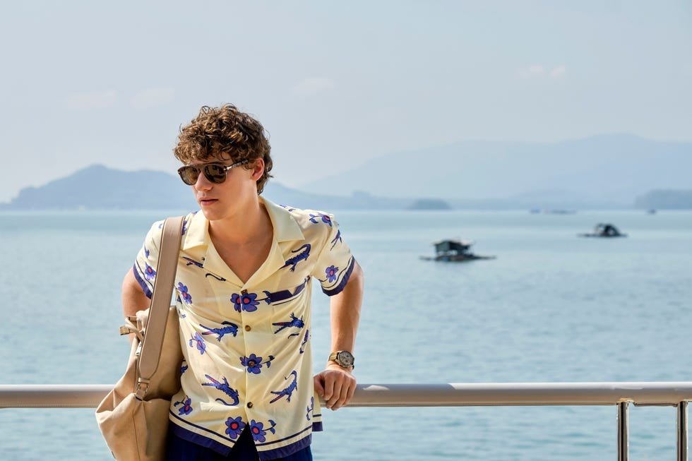 man wearing sunglasses and leaning against a railing with an ocean view in the background