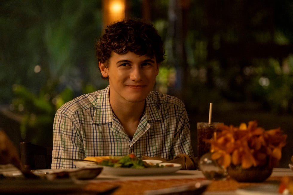 a young person seated at a table surrounded by food and drinks