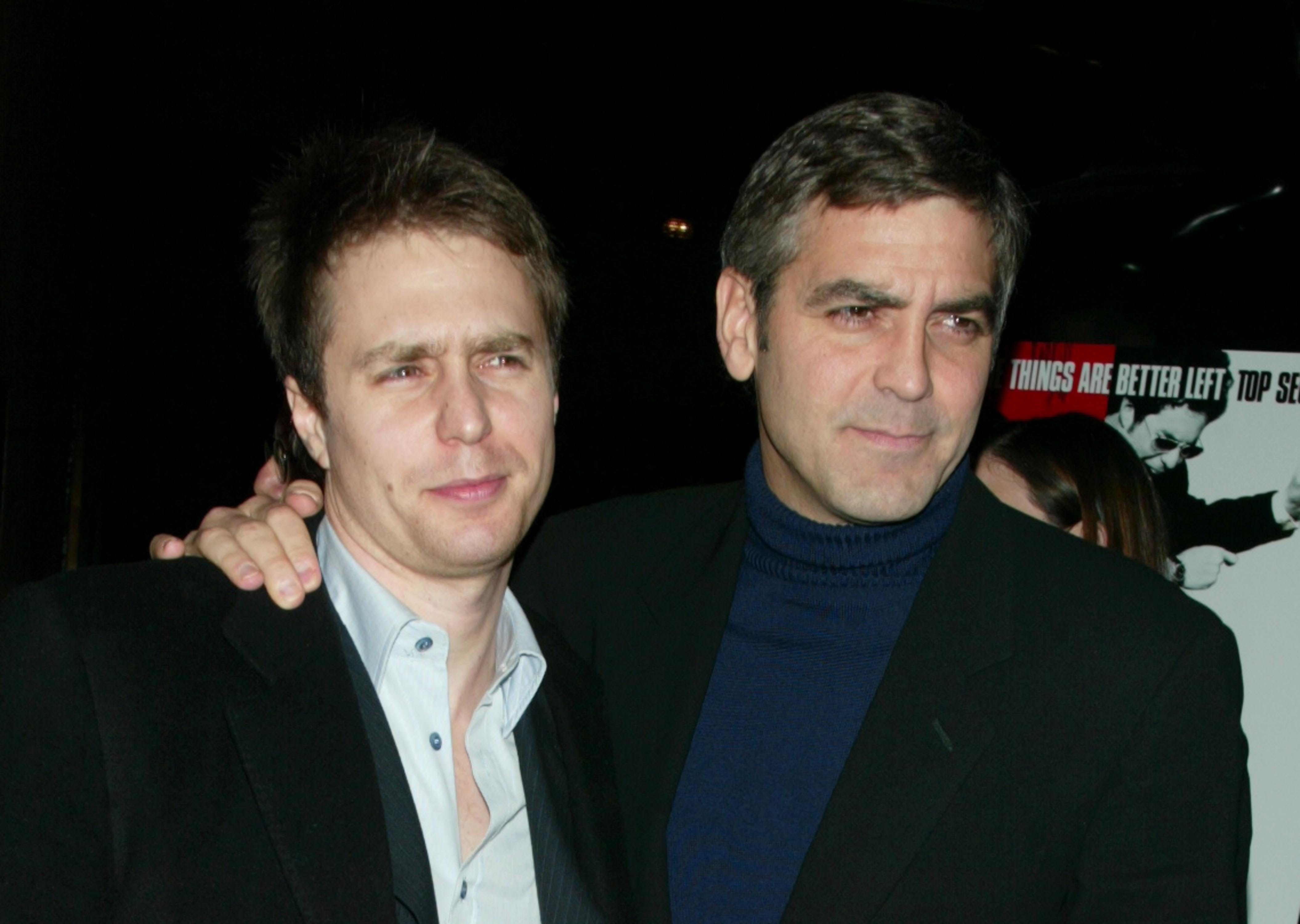 sam rockwell and george clooney stand together for photos and look to the right, both men wears black suit jackets
