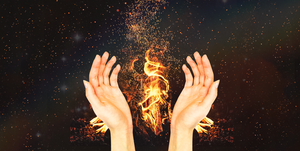 a pair of white hands are held open and semi cupped in front of a bonfire on a black background