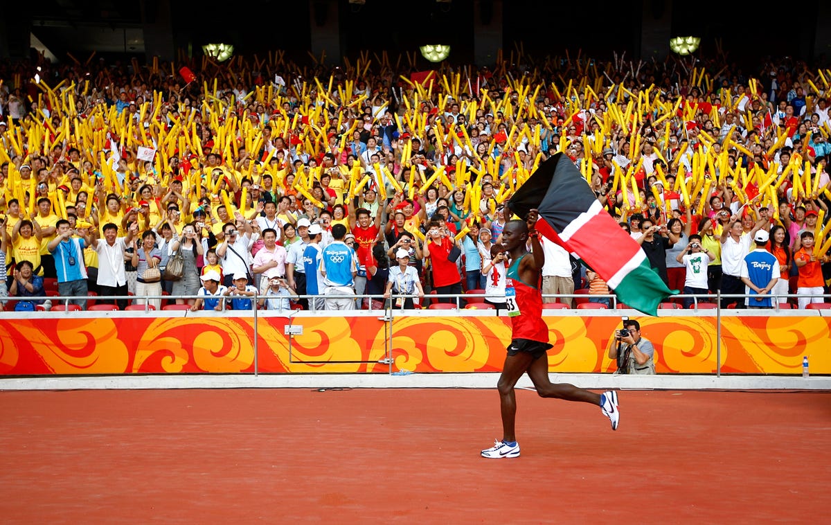 sammy wanjiru celebra su victoria en el maratón de los juegos olímpicos de pekín elevando al aire la bandera de kenia ante cientos de espectadores en las gradas tras batir el récord olímpico de la prueba