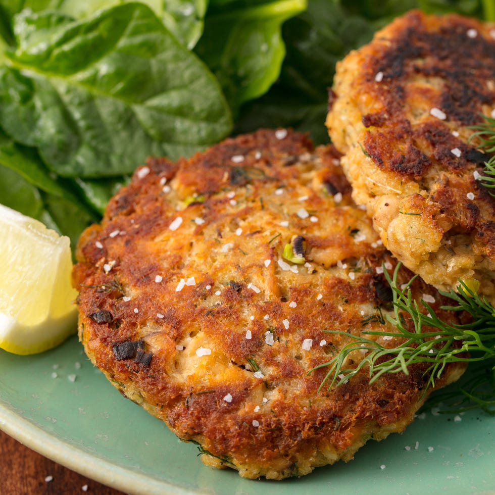 plate of golden brown salmon patties served with fresh spinach and lemon