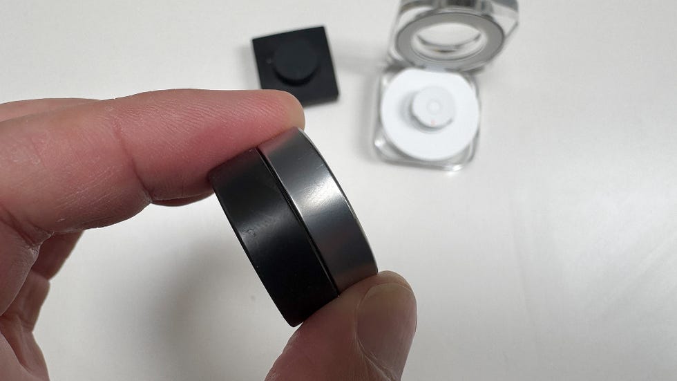 a hand holding a black and a silver smart ring side by side for comparison