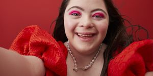 close up of smiling young woman with down syndrome taking selfie against red background
