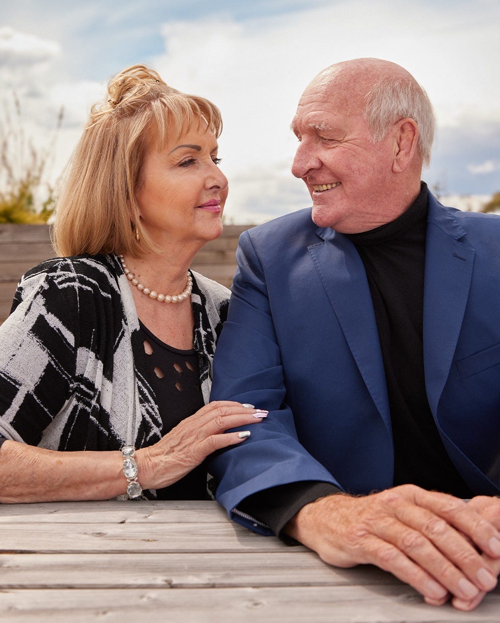elderly couple seated at a wooden table displaying affection