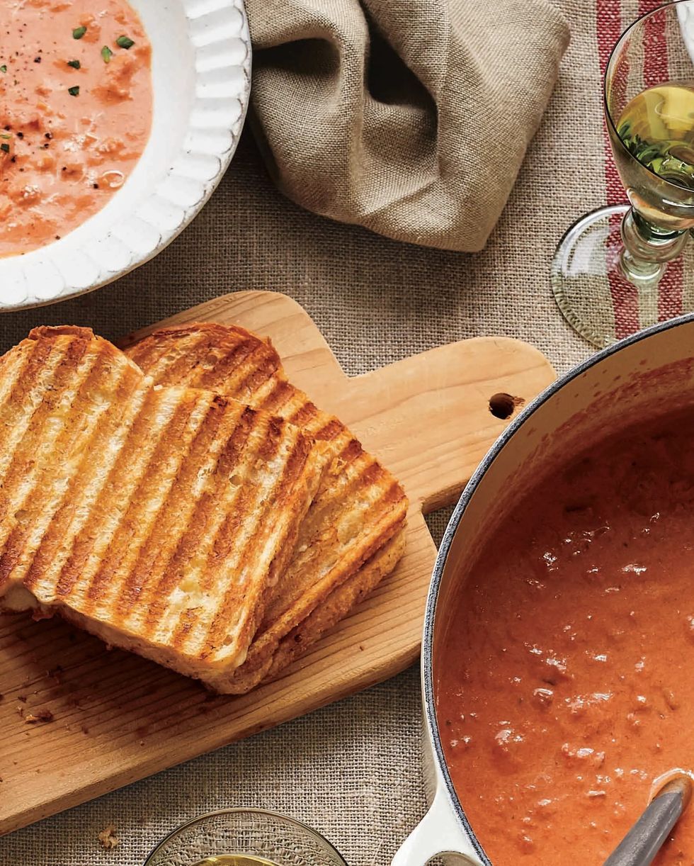 cheddar chutney grilled cheese sandwiches on a wooden serving board next to bowls on tomato soup