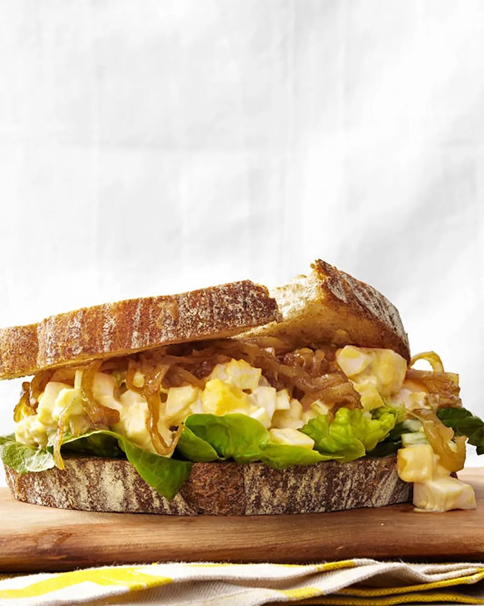 egg salad sandwich with caramelized onions on a wooden serving board