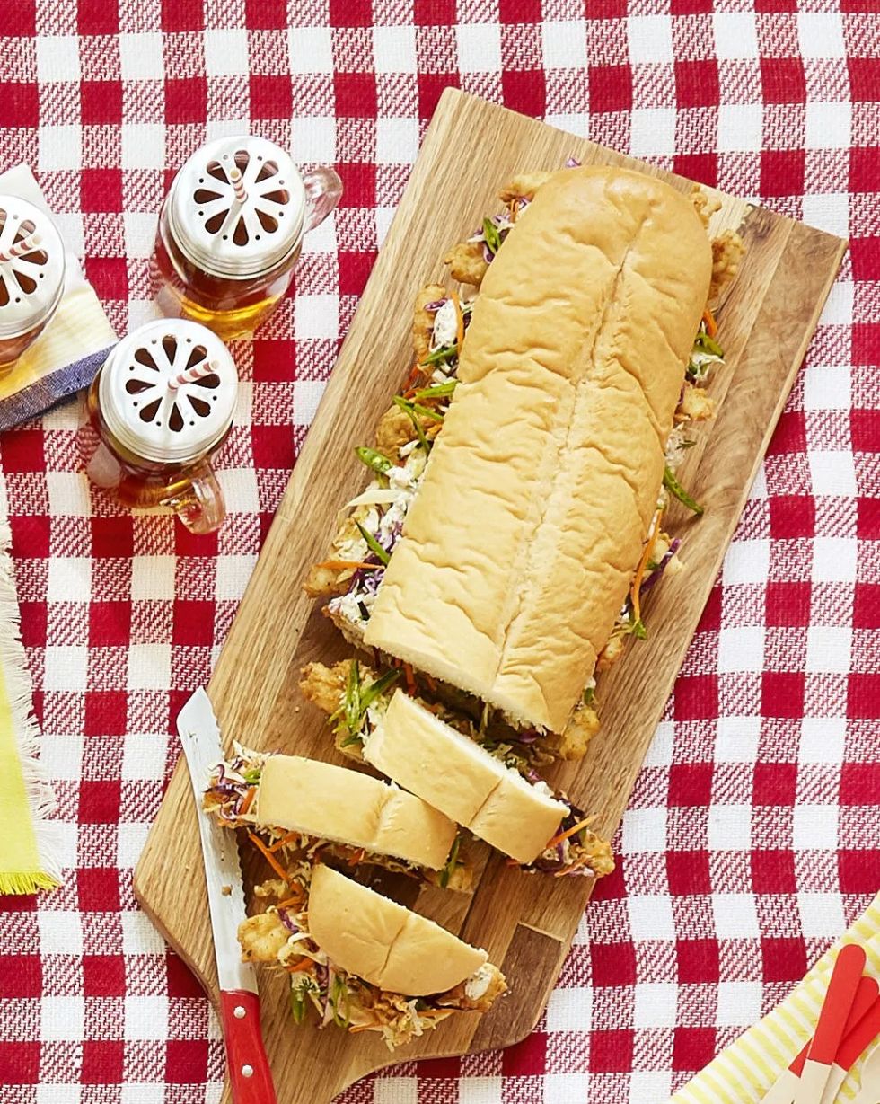 chicken finger sub sandwich with one end cut into slices all on a wooden serving board on a red and white checkered picnic blanket