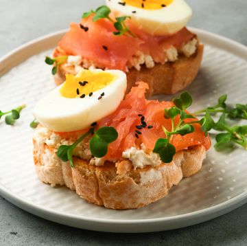 sandwich with delicious toppings smoked salmon, eggs, herbs and microgreens radish, black sesame seeds over white plate on gray concrete table background. healthy open sandwich superfood. top view.