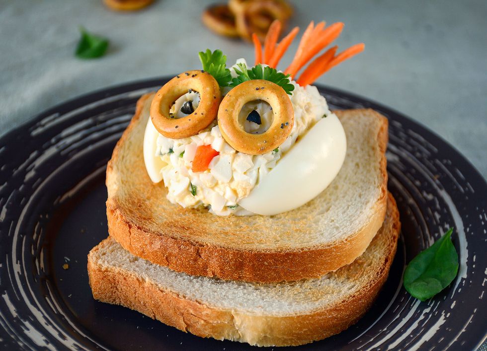 rebanadas de pan de molde tostadas con una bola de ensaladilla y huevo duro decoradas con una cara divertida