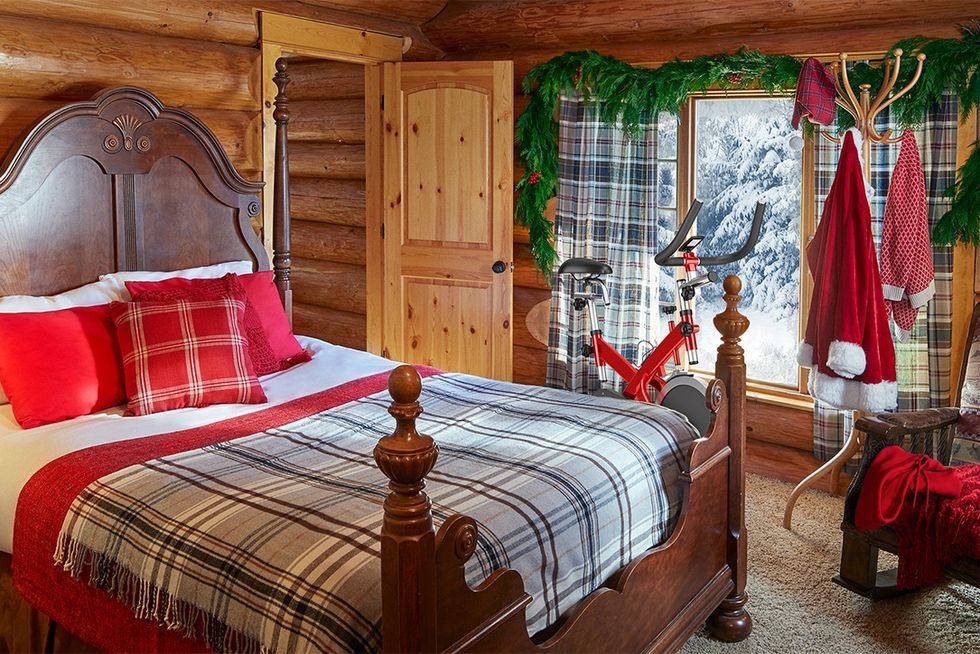 log cabin bedroom with antique wood bed, plaid blankets and curtains, evergreen window garland, coat rack santa's winter gear