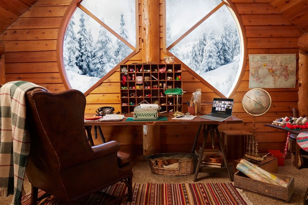 santa's log cabin home office with maps, globe, typewriter, laptop, and semicircle window overlooking snowy forest