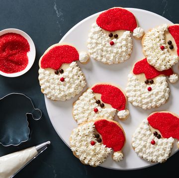 sugar cookies decorated like santa claus with white frosting, red sprinkles, and chocolate for eyes