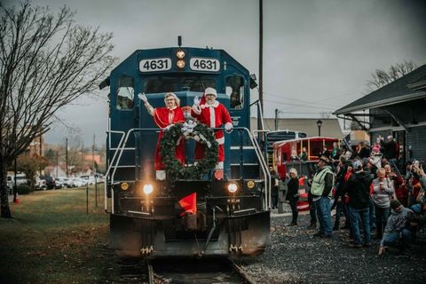 train pulling into the station, where people are waiting, with santa and mrs claus standing at the front of the train waving to everyone