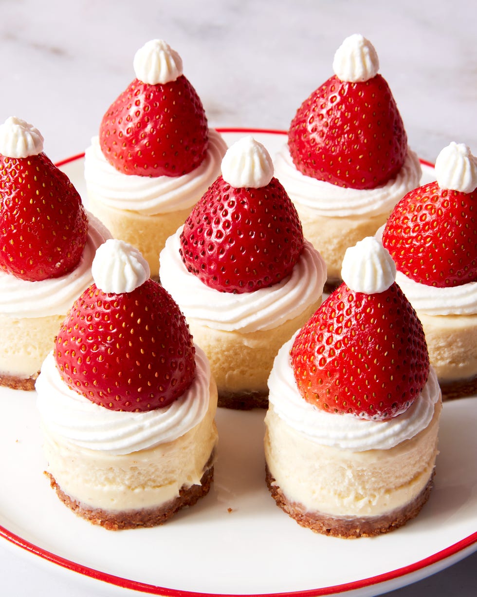 mini cheesecake bites topped with strawberries and whipped cream to look like a santa hat