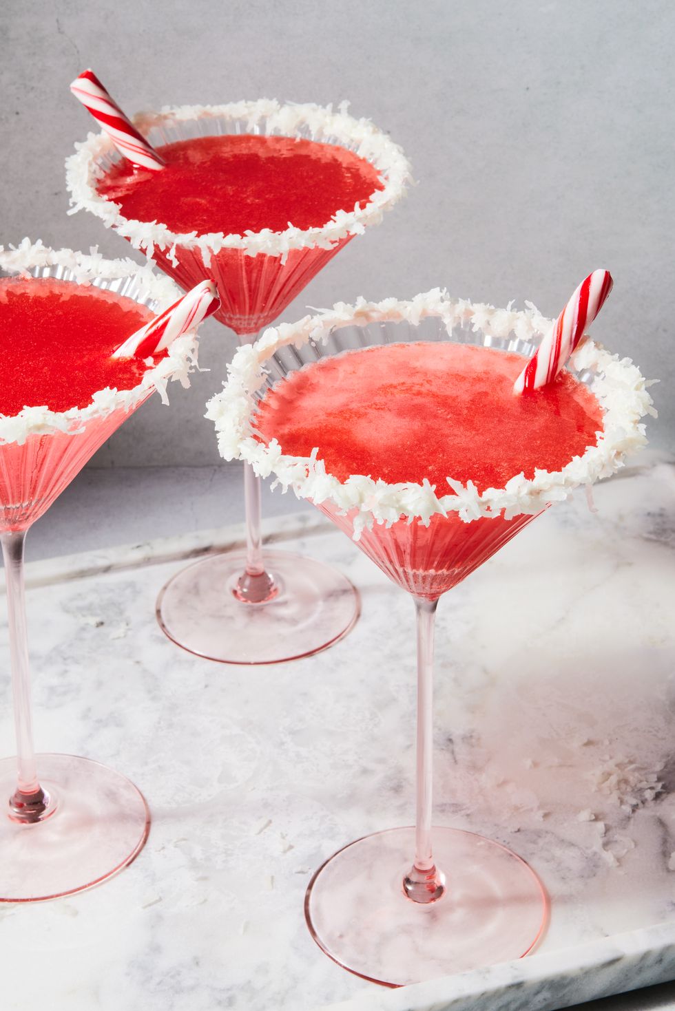 red cocktail with a coconut rim and peppermint stick garnish