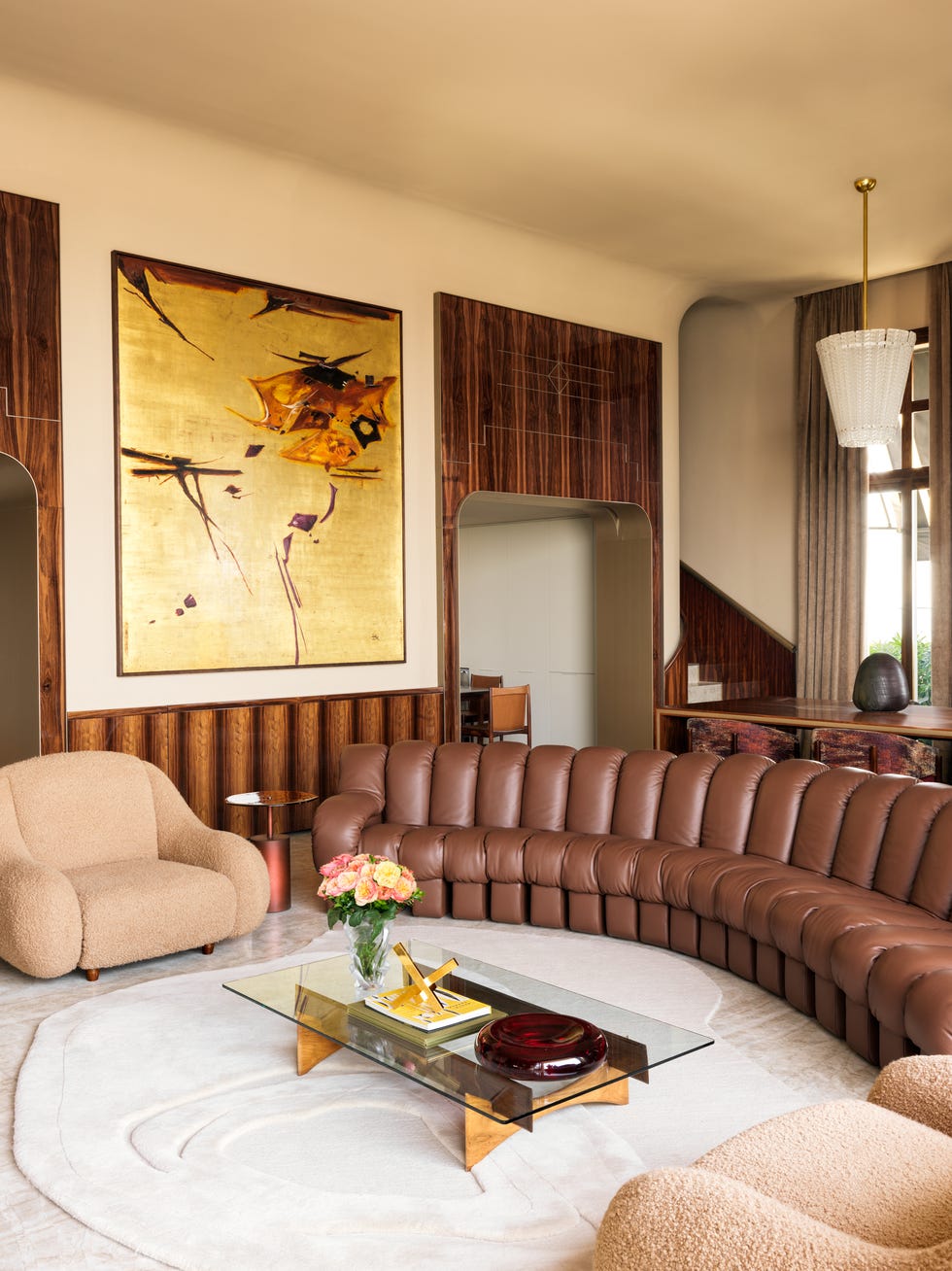 the living area featuring a brown sofa and two camel colored chairs on a white carpet