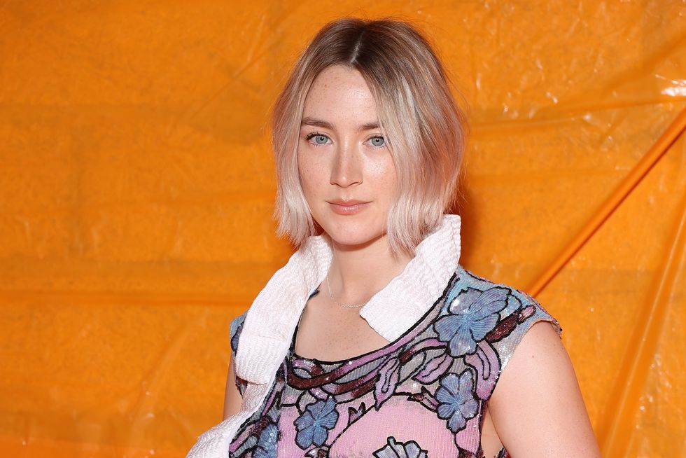 saoirse ronan, a woman with blond hair in a bob stands looking at the camera wearing a floral sequin dress