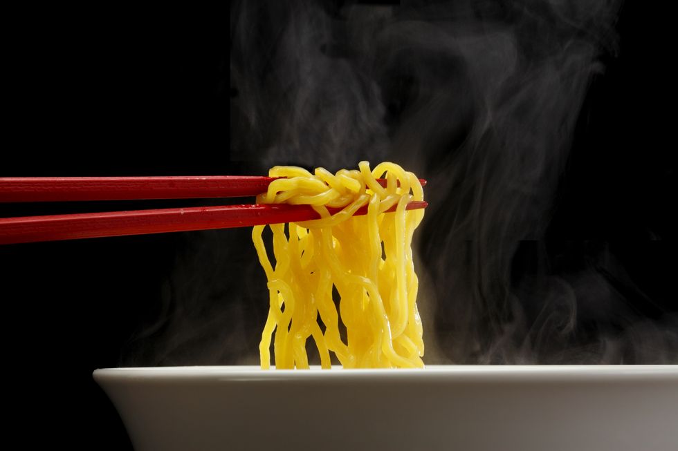 sapporo ramen noodle lifted up by red chopsticks with steam against black background