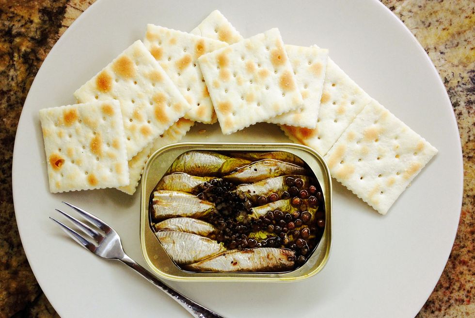 sardines in olive oil and peppercorns in a can with saltine crackers and a fork on a plate