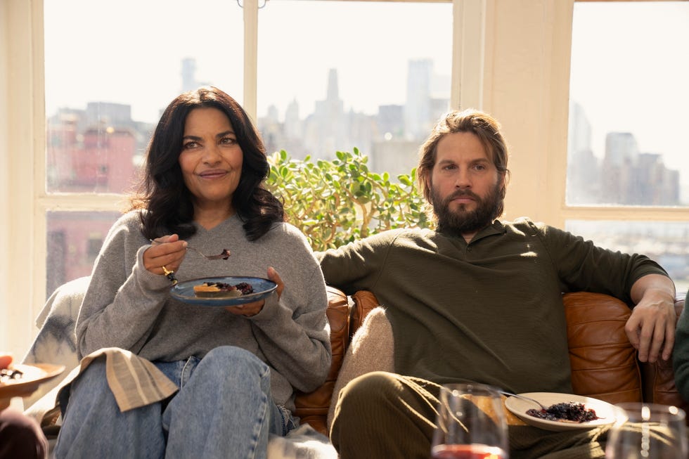 two people sitting on a couch with plates of food enjoying a sunny day indoors