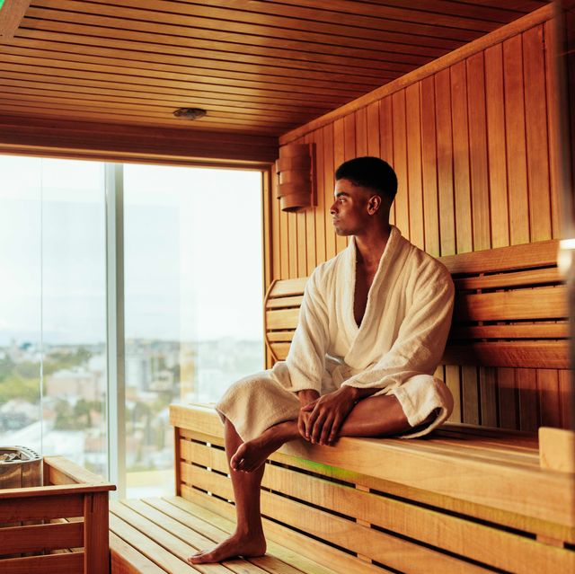 a young african american man is wearing a bathrobe and enjoying the view of the city in the sauna