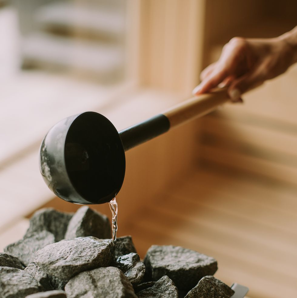 young woman hand pouring water on hot rocks in the sauna