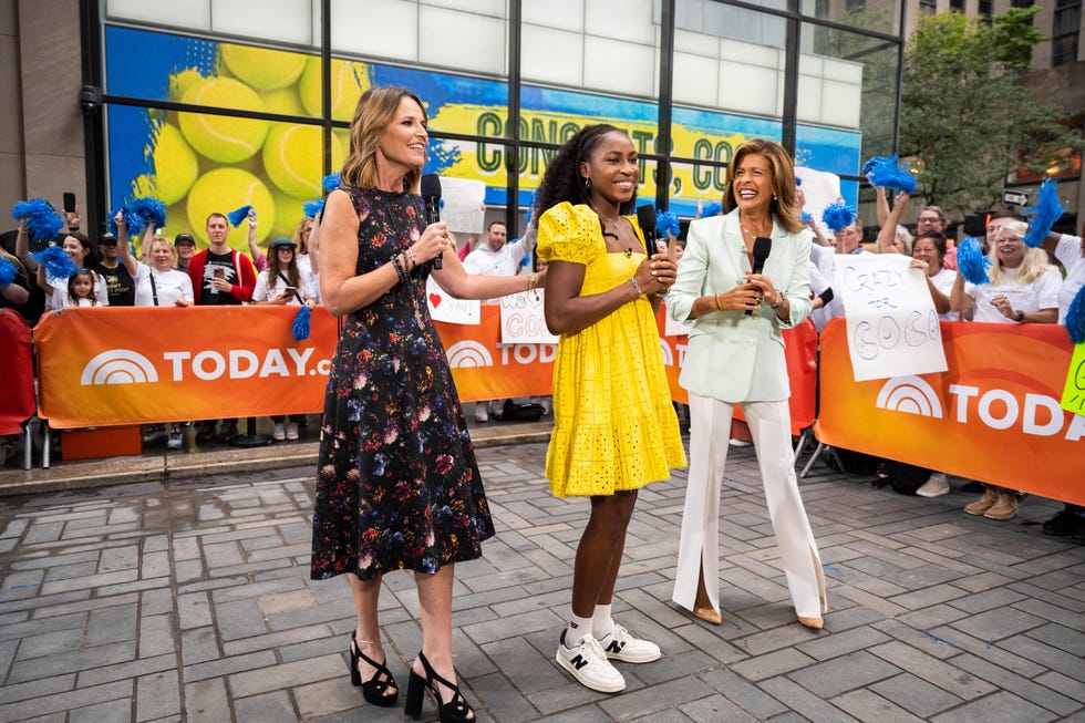 savannah guthrie, coco gauff, and hoda kotb stand on a city street and smile while holding microphones, crowds of people watch from behind orange fences