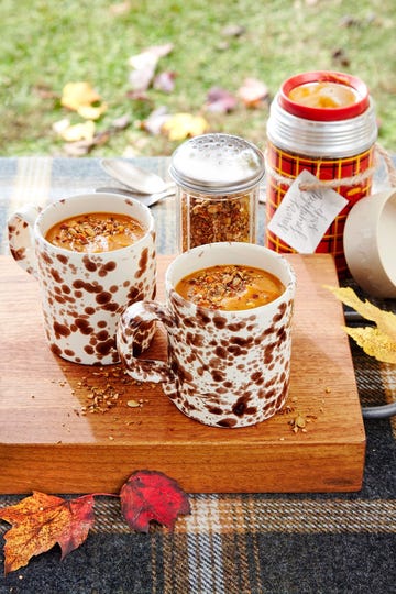 brown and white speckled mugs with soup inside, topped with granola on a wooden board