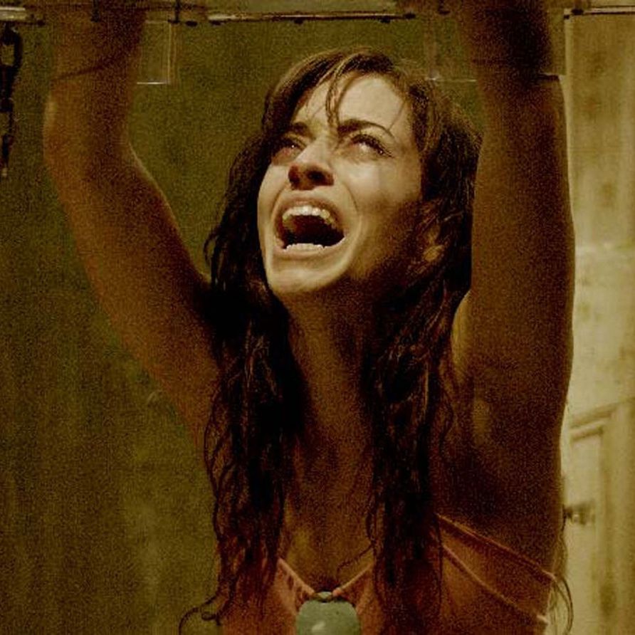 a woman reaches up into a glass jigsaw trap in a scene from saw ii