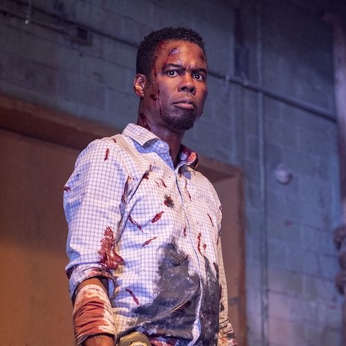 a man played by chris rock stands, bloodied, in a scene from spiral