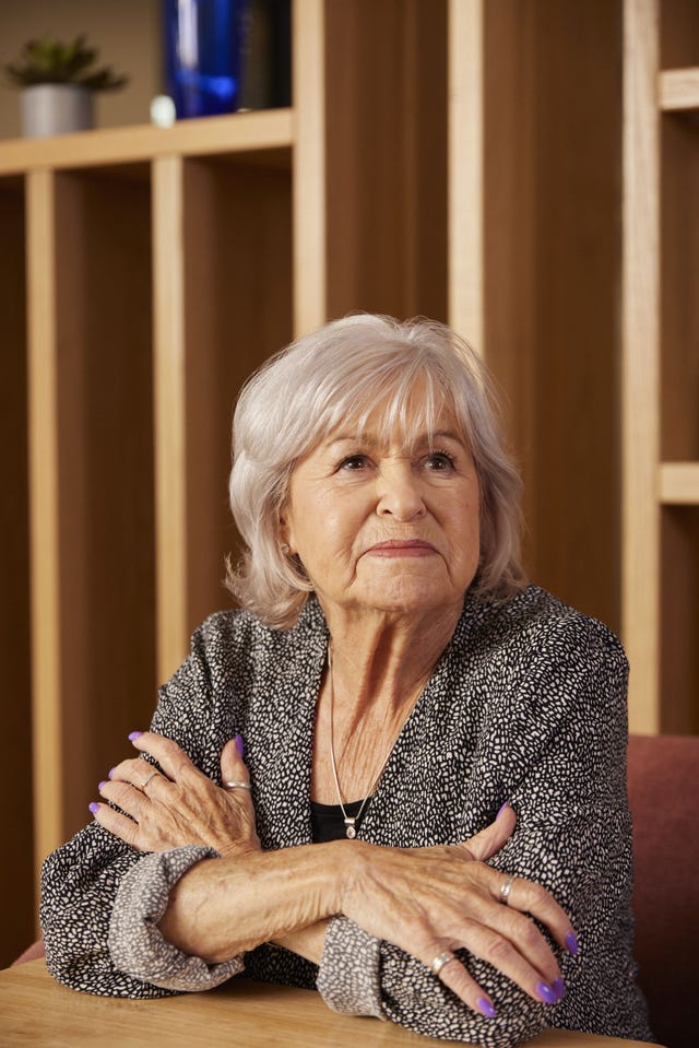 older lady with short grey hair indoors looking wistfully into distance