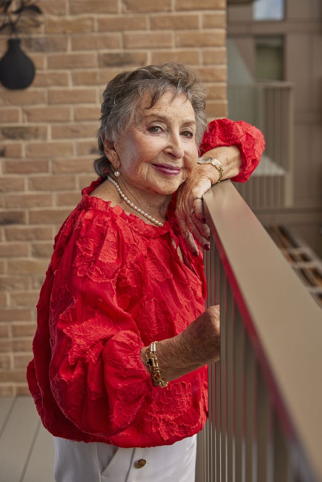 older smiling lady in red top looking out over a balcony