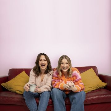 natalie cassidy and joanna page sitting on a red couch in front of a pink wall