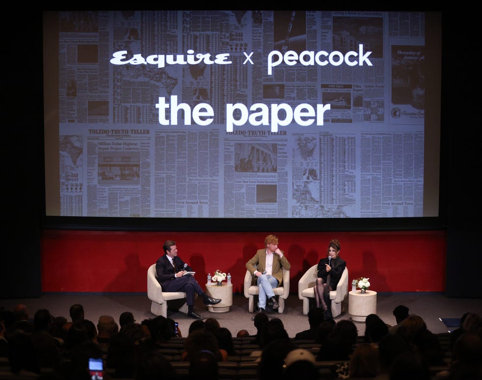 painel de discussão com indivíduos no palco com uma tela exibindo fundos de jornais impressos