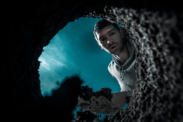 scared guy digging a deep earthen hole with a shovel during a moonlit night